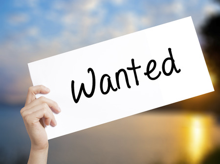 Wanted Sign on white paper. Man Hand Holding Paper with text. Isolated on sunset background.  Business concept. Stock Photoの写真素材