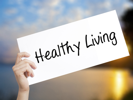 Healthy Living  Sign on white paper. Man Hand Holding Paper with text. Isolated on sunset background.  Business concept. Stock Photoの写真素材