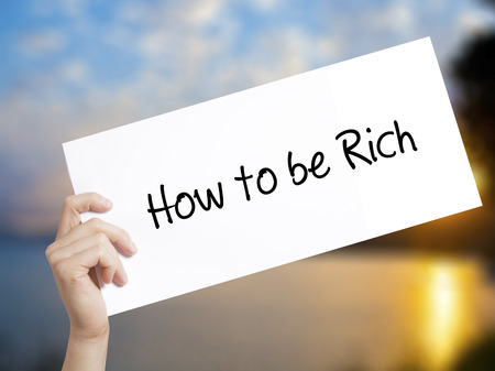 How to be Rich  Sign on white paper. Man Hand Holding Paper with text. Isolated on sunset background.  Business concept. Stock Photoの写真素材