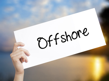 Offshore Sign on white paper. Man Hand Holding Paper with text. Isolated on sunset background.   Business concept. Stock Photoの写真素材