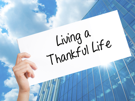 Living a Thankful Life Sign on white paper. Man Hand Holding Paper with text. Isolated on Skyscraper background.  technology, internet concept.の写真素材