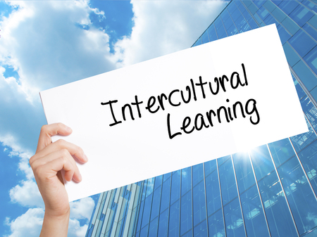 Intercultural Learning Sign on white paper. Man Hand Holding Paper with text. Isolated on Skyscraper background.   Business concept. Stock Photoの写真素材