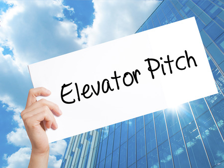 Elevator Pitch Sign on white paper. Man Hand Holding Paper with text. Isolated on Skyscraper background.   Business concept. Stock Photoの写真素材