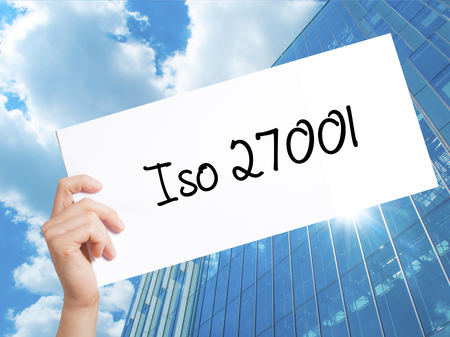 Iso 27001  Sign on white paper. Man Hand Holding Paper with text. Isolated on Skyscraper background.   Business concept. Stock Photoの写真素材