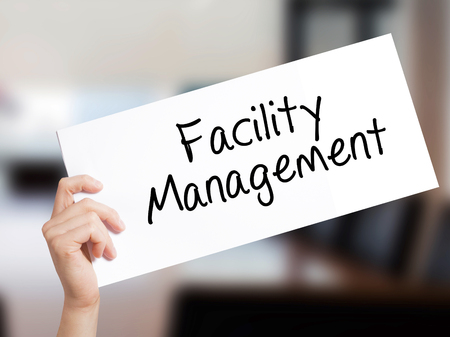 Facility Management Sign on white paper. Man Hand Holding Paper with text. Isolated on Office background.   Business concept. Stock Photoの写真素材