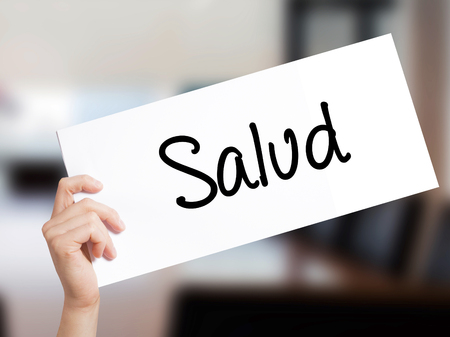 Salud (Health in Spanish) Sign on white paper. Man Hand Holding Paper with text. Isolated on Office background.  Business concept. Stock Photoの写真素材