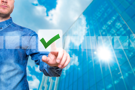 Young male hand touching, pressing modern button and ticking check box out of empty boxes on digital screen interface. Isolated on blurred skyscraper. Business technology concept. Stock Imageの写真素材