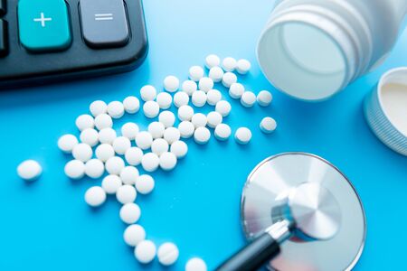 Calculator, pills and sthetoscope on blue background. cost of health care conceptの写真素材
