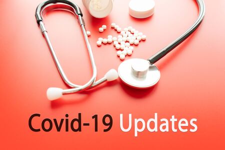 Stethoscope, magnifying glass with words CORONAVIRUS UPDATES on red background. Covid-19 concept and coronavirusの写真素材