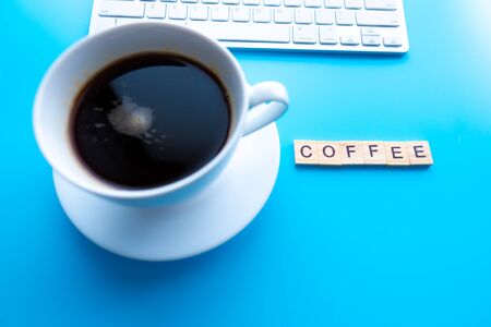 Text Coffee. Flat lay, top view office table desk. Workspace with  keyboard, office supplies, and coffee cup on blue background.の写真素材