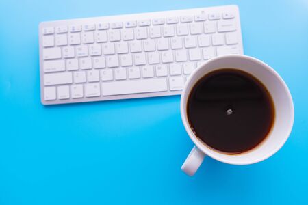 Creative flat lay photo of workspace desk. Top view office desk with keyboard and coffee cup on blue color background.の写真素材