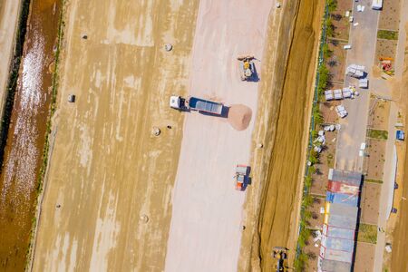 Aerial photo of bulldozer pours sand into the truck. On the construction site top view. Shooting...
