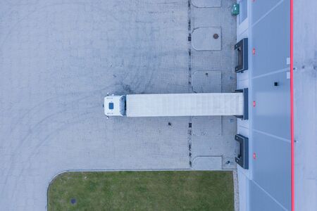 Aerial view of goods warehouse. Logistics center in industrial city zone from above. Aerial view of trucks loading at logistic centerの写真素材