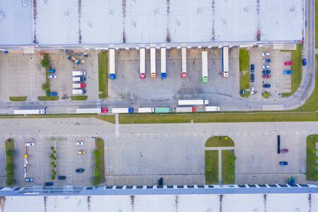 Aerial view of goods warehouse. Logistics center in industrial city zone from above. Aerial view of trucks loading at logistic center. View from drone.の写真素材