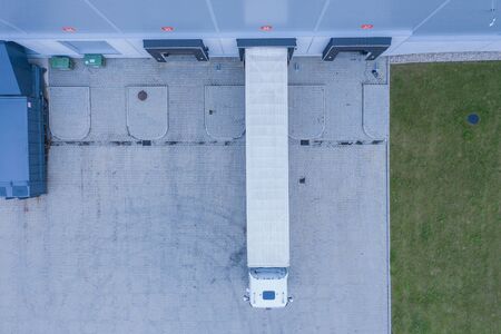 Aerial view of goods warehouse. Logistics center in industrial city zone from above. Aerial view of trucks loading at logistic centerの写真素材