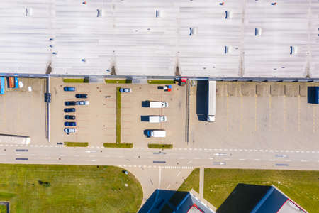 Aerial view of goods warehouse. Logistics center in industrial city zone from above. Aerial view of trucks loading at logistic centerの写真素材