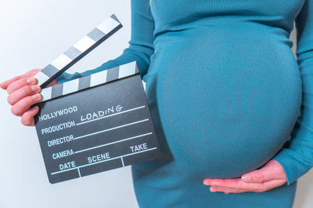 Pregnant woman holding movie clapperboard isolated on white