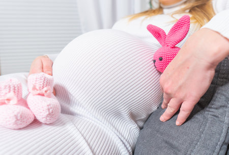 Two small bunny shoes at the hand of pregnant woman. Pregnant woman getting ready for child's bornの写真素材