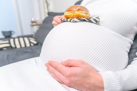 Pregnancy and unhealthy eating concept: pregnant woman holds a plate with tasty donuts in her handの写真素材