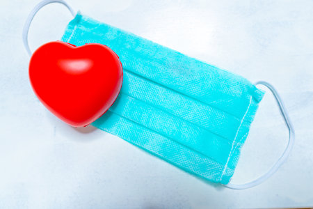 Disposable medical mask on blue background with red heart on it against bacteria and viruses. Stop the spread of coronavirus, self-defense. Copy spaceの写真素材
