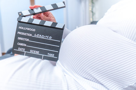 Pregnant woman hands holding clapper board on her belly. With Loading signの写真素材