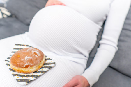 Pregnancy and unhealthy eating concept: pregnant woman holds a plate with tasty donuts in her handの写真素材