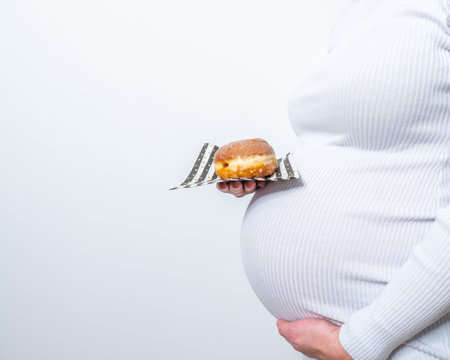 Pregnancy and unhealthy eating concept: pregnant woman holds a plate with tasty donuts in her handの写真素材