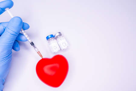 a hand in a medical glove holds an ampoule containing the covid-19 vaccine, invented to prevent the spread of the virus around the world. mask with a red heart on a white backgroundの写真素材