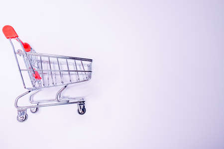 Side profile half turned close up view photo of tiny small silver and red metallic with wheels empty push cart isolated on bright white background copyspaceの写真素材