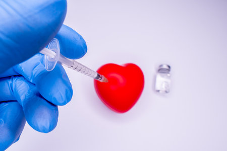 a hand in a medical glove holds an ampoule containing the vaccine, invented to prevent the spread of the virus around the world. mask with a red heart on a white backgroundの写真素材