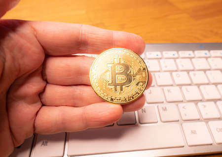 Fingers hold a gold bitcoin on the keyboard background