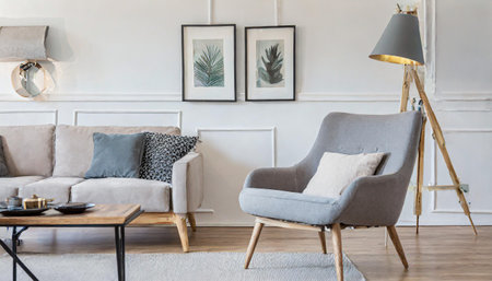 Gray armchair near beige loveseat sofa against white wall with poster frames. Japandi home interior design of modern living room.の素材