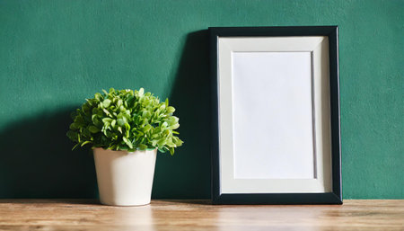 Blank picture frame mockup with green plant in pot on wooden tableの素材