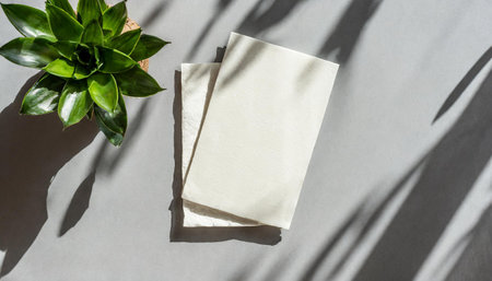 the mockup overlay weaves in shadows from an exotic plant, as natural light two vertical sheets of textured white paper resting on a soft gray table background. with leavesの素材