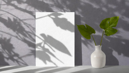 vertical sheets of textured white paper against a soft gray table background. the natural light creates subtle shadows from an exotic plant, enhancing the mockup overlay in a horizontalの素材