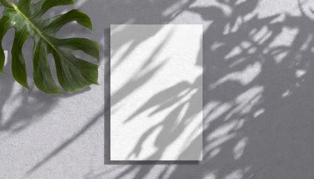 vertical sheets of textured white paper against a soft gray table background. the natural light creates subtle shadows from an exotic plant, enhancing the mockup overlay in a horizontalの素材