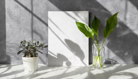 vertical sheets of textured white paper against a soft gray table background. the natural light creates subtle shadows from an exotic plant, enhancing the mockup overlay in a horizontalの素材