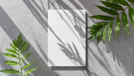 vertical sheets of textured white paper against a soft gray table background. the natural light creates subtle shadows from an exotic plant, enhancing the mockup overlay in a horizontalの素材