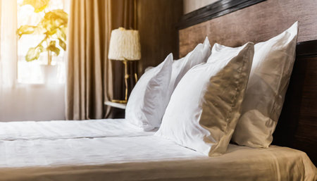 Bed maid-up with clean white pillows and bed sheets in beauty room. Close-up. Lens flair in sunlight,imageの素材