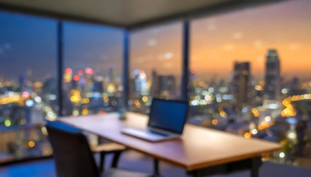 A softly lit office workspace interior captured in the evening with a cityscape backdrop. The blurred design highlights a professional, modern business environment perfect for work, meetings,の素材