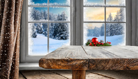 An inviting empty wooden table set against the backdrop of a frosty winter window, showcasing a snow-covered landscape. The image captures the peaceful charm of winter, ideal for seasonal decorの素材