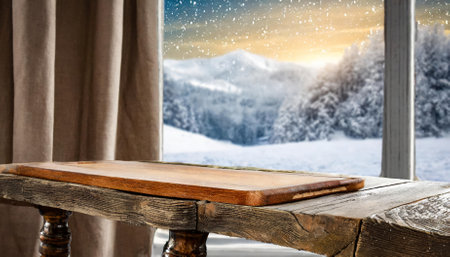 An empty wooden table in focus with a frosty winter window blurred in the background. Captures a serene, cozy winter ambiance, ideal for festive projects, seasonal designs, or product stagingの素材