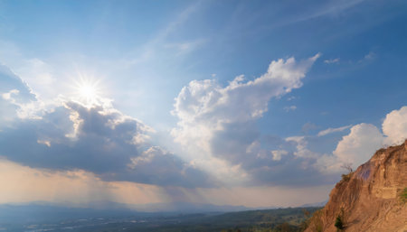 This stunning photograph captures the radiant light of the sun bathing the sky, which boasts a vivid blue hue. The scene features an artful mix of small and large clouds dispersed in alternatingの素材