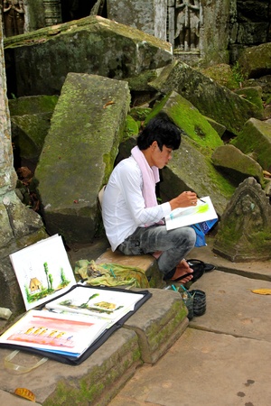 SIEMREAP, KHMER REPUBLIC - NOVEMBER 6 : The unidentified artist is sitting on the stone under the big tree in very popular corner of Ta Prohm Temple and drawing a picture for sell on November 6, 2011 at Ta Prohm Temple, Siemreap, Khmer Republic.のeditorial素材