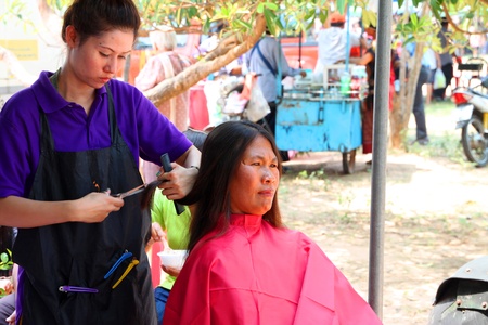 NACHUAK, MAHASARAKHAM - MARCH 21 : The unidentified barber is cutting an old woman hair in public secter services mobile project on March 21, 2012 at Nong Bua Daeng school court, Nachuak, Mahasarakham, Thailand.のeditorial素材