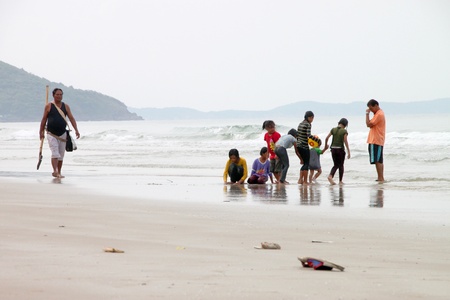 BAN PHE, RAYONG - MAY 10 : Unidentified man is cleaning sand beach while tourists are playing on May 10, 2012 at Ban Phe sea shore, Rayong, Thailand.のeditorial素材
