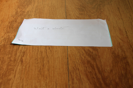 " wait a minute " handwritten on note paper on wooden floorの写真素材