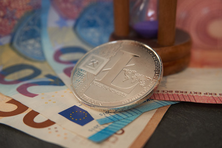 Silver litecoin and hourglass  lying on the  euro notes, grey stone background. Cryptocurrency digging speed concept, selective focus.の写真素材