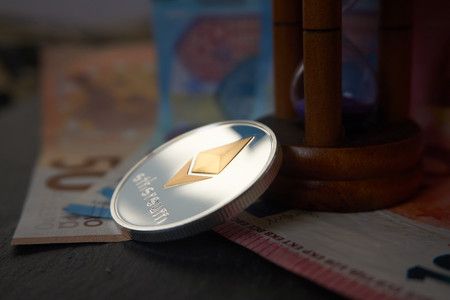 Silver Ethereum coin and hourglass  lying on the  euro notes, grey stone background. Cryptocurrency digging speed concept, selective focus.の写真素材