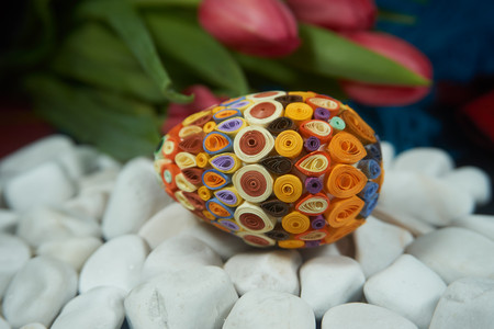 Hand-crafted Easter egg on the surface of white stones near of red tulips. Easter decor, selective focus.の写真素材